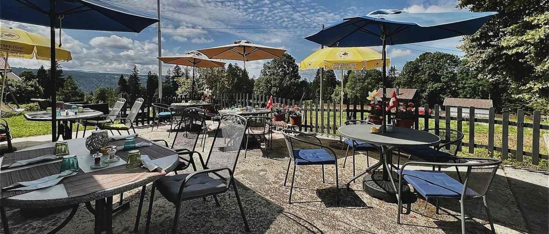 Terrasse de restaurant Les Cernets avec vue sur la nature du Jura suisse et drapeau Suisse