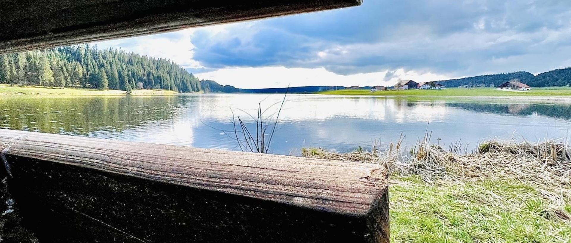 Vue paisible du lac des Taillères depuis un banc en bois, nature du Val de Travers Jura suisse