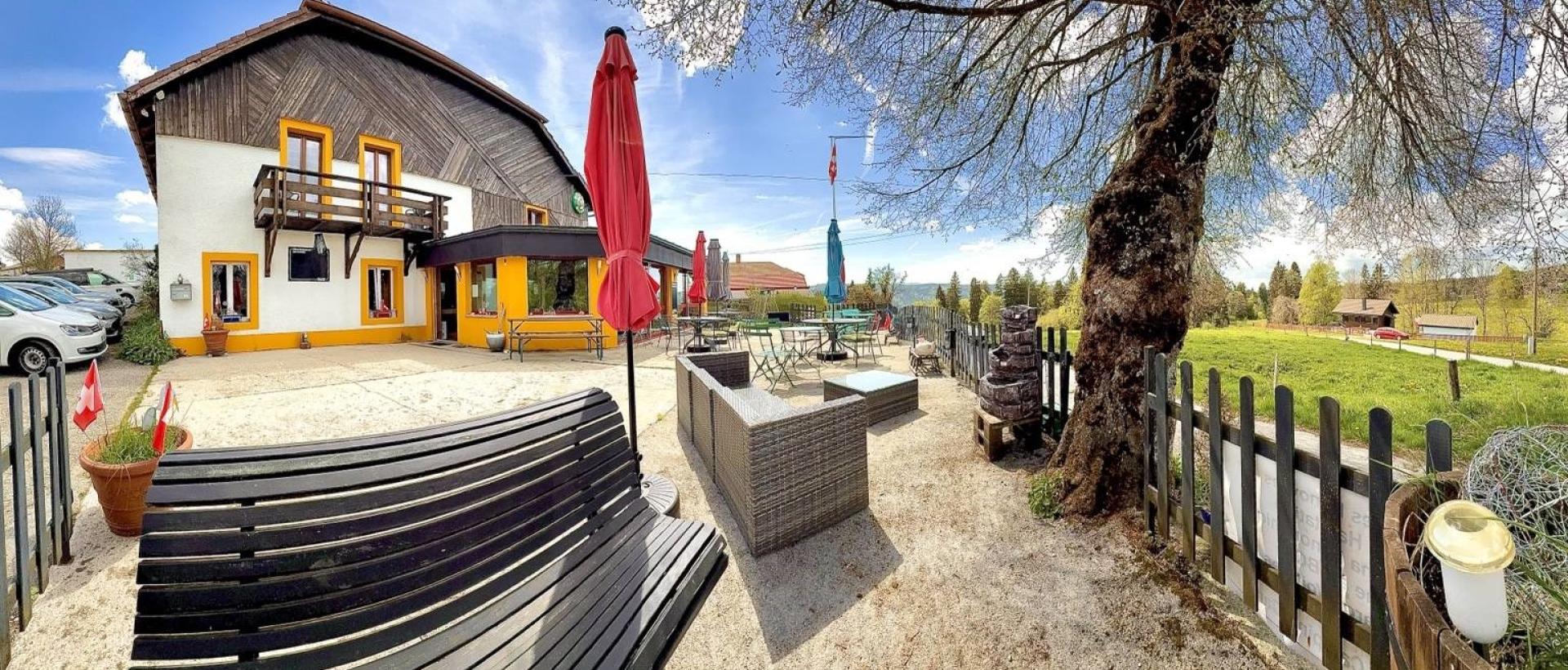 Terrasse ensoleillée de l'Hôtel Restaurant Les Cernets au Val-de-Travers dans le Jura suisse avec vue nature et espace détente extérieur