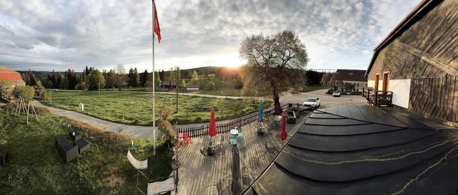 Hôtel Les Cernets avec vue sur la campagne du Val de Travers et drapeau suisse dans un cadre naturel du Jura suisse