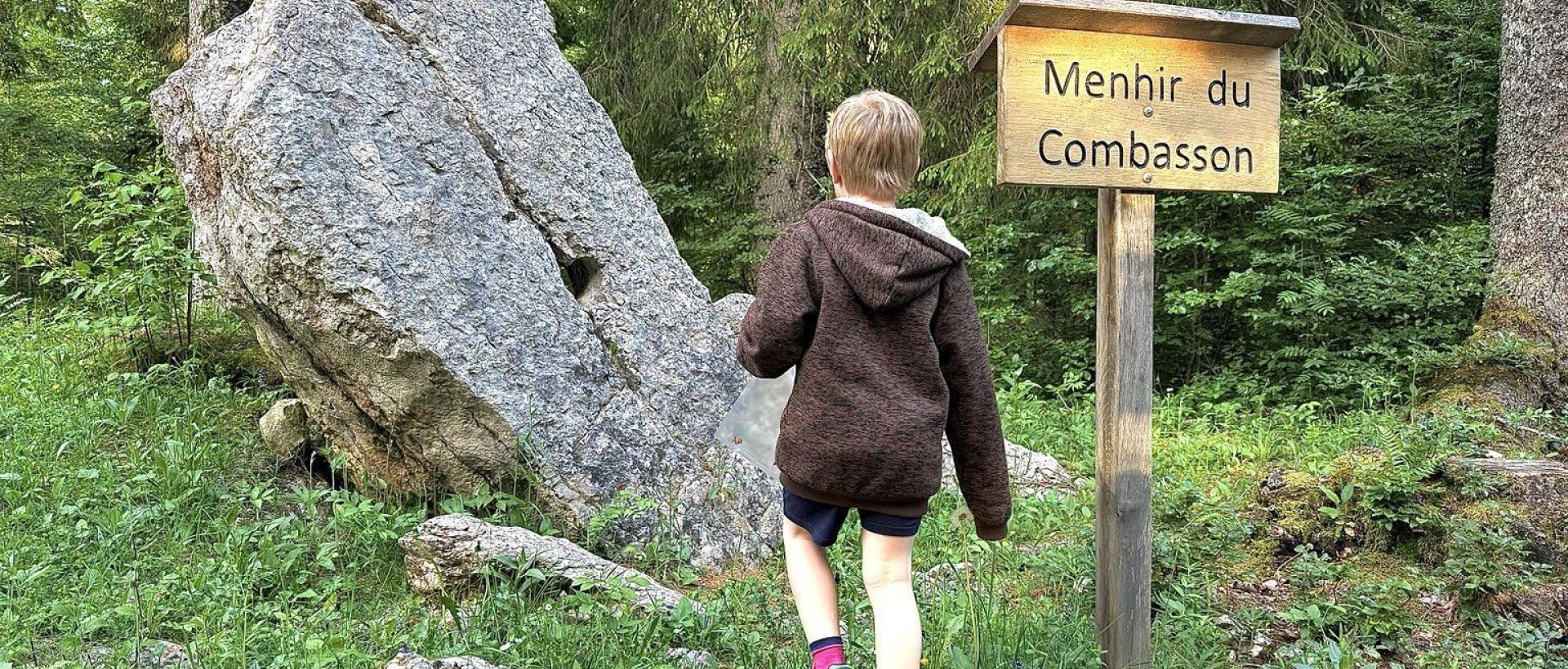 Enfant découvrant le Menhir du Combasson près des Cernets, site historique et curiosité naturelle du Val de Travers dans le Jura suisse