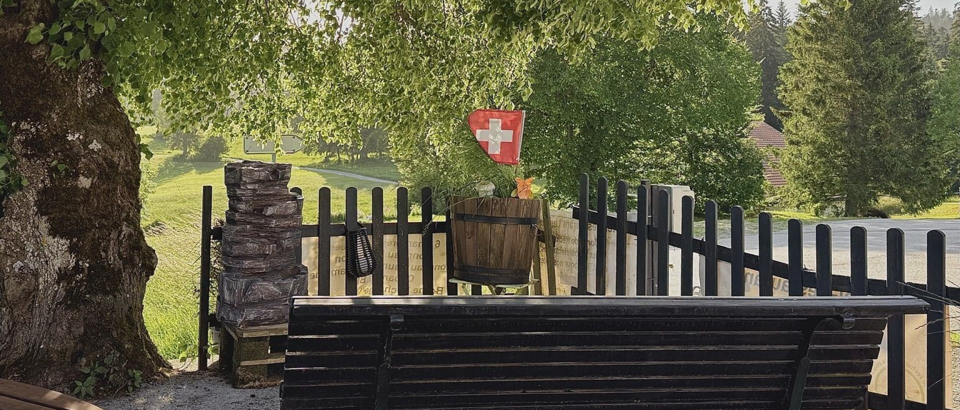 Terrasse avec un banc et drapeau Suisse, calme et sérénité aux Cernets Val de Travers