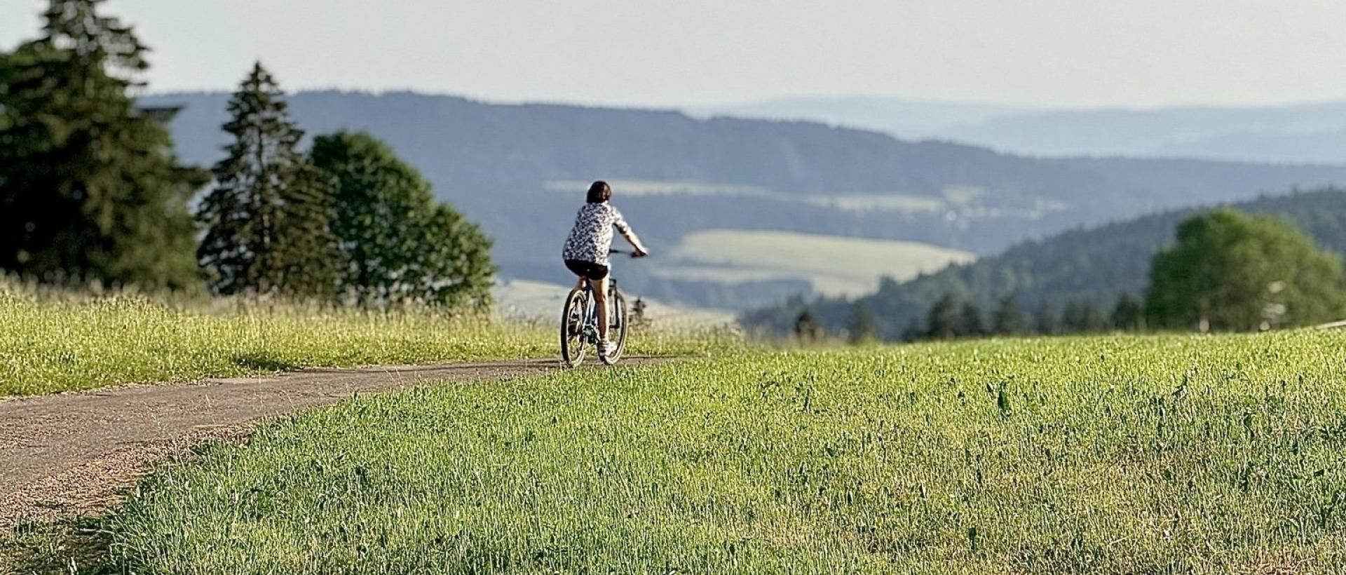 Cycliste sur les routes panoramique du Jura suisse entre les Cernets et la Vallée de la Brévine avec vue sur les paysages de la France voisine