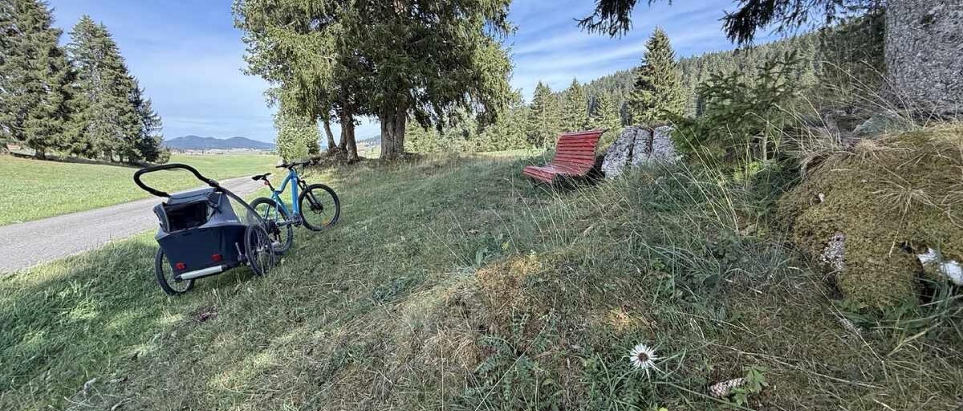 Vélo avec remorque près d'un banc dans la nature aux Cernets, entre le Val-de-Travers et vallée de la Brévine, Jura suisse