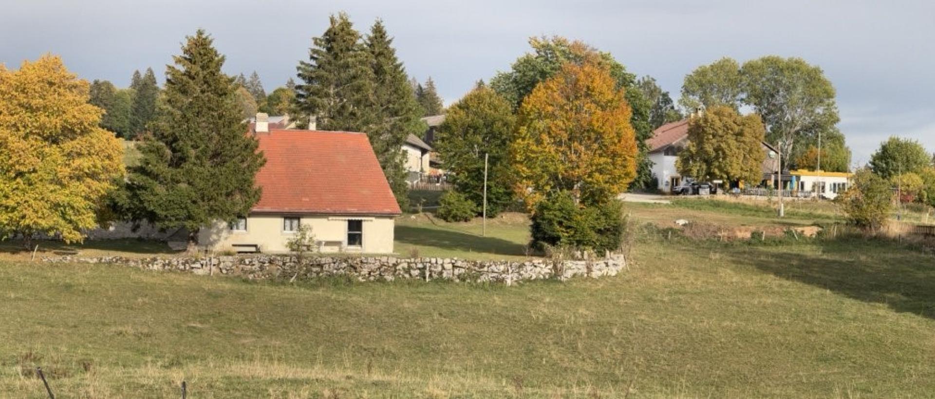 Panorama de campagne aux Cernets, dans le Val-de-Travers, avec pâturages, Hôtel, arbres aux couleurs d'automne, dans le Jura neuchâtelois