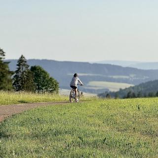 Cycliste sur les routes panoramique du Jura suisse entre les Cernets et la Vallée de la Brévine avec vue sur les paysages de la France voisine